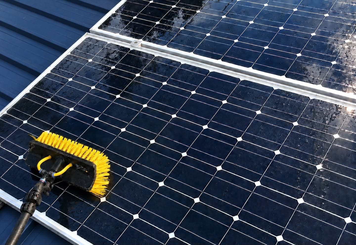 Solar panels being washed with a long-handled soft brush